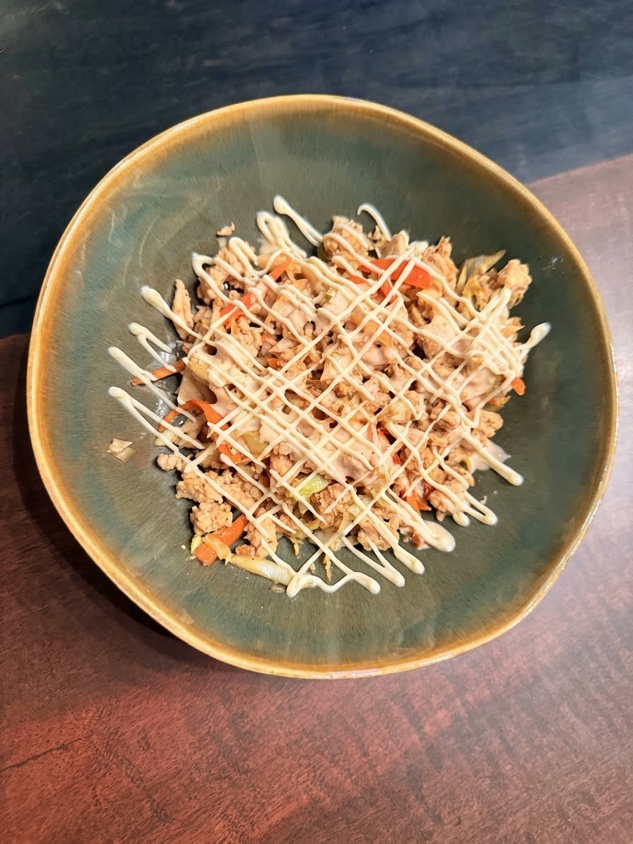 A green ceramic bowl of ground turkey egg roll in a bowl with shredded cabbage and carrots, drizzled in a criss-cross pattern with creamy sriracha sauce